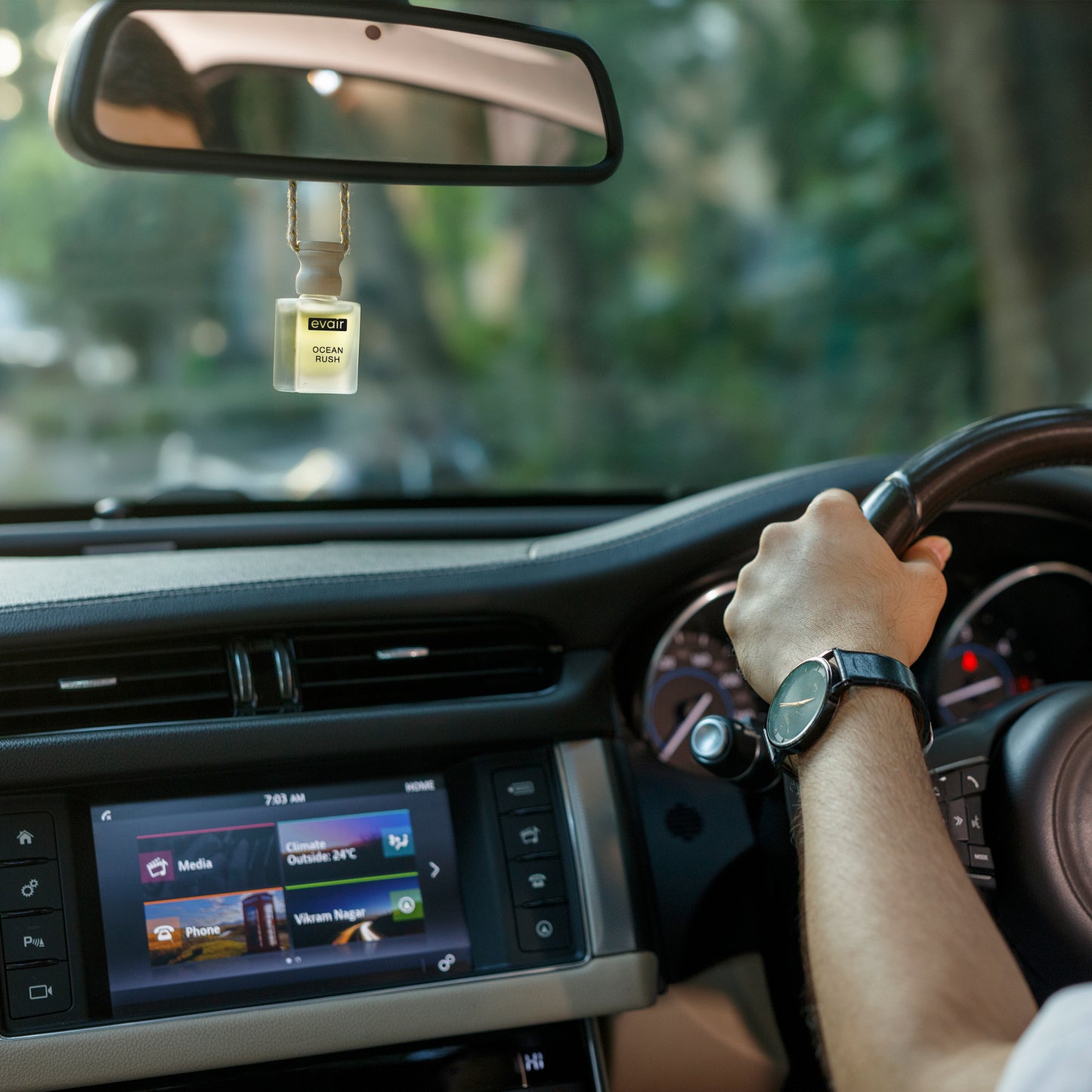 Man driving a car with an Evair Ocean Rush car freshener hanging from the rearview mirror.
